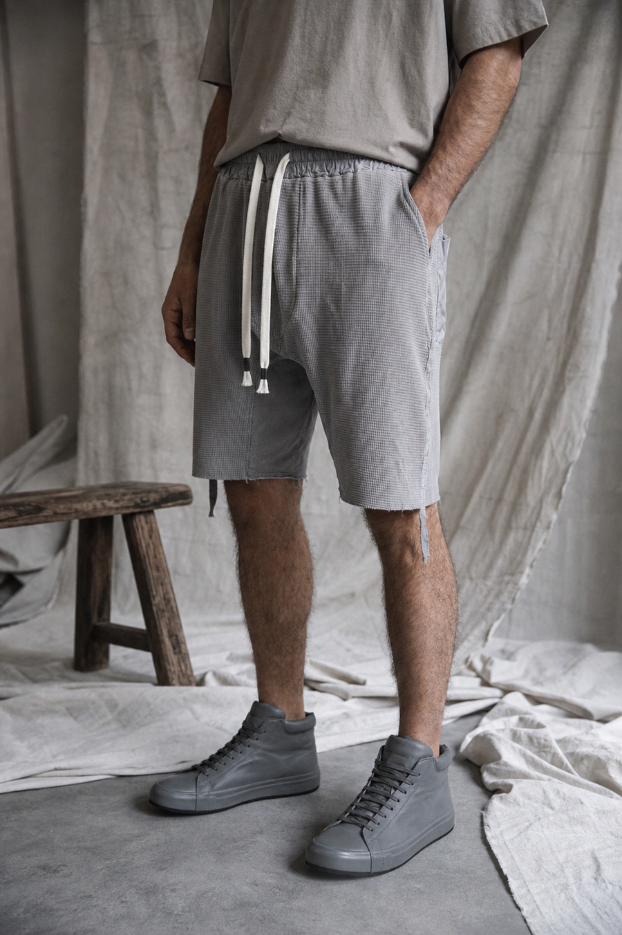 AITO Textured Drop-Crotch Shorts in Grey — three-quarter front view on model, hand in the deep side pocket, showing the waffle-knit texture and white drawstring