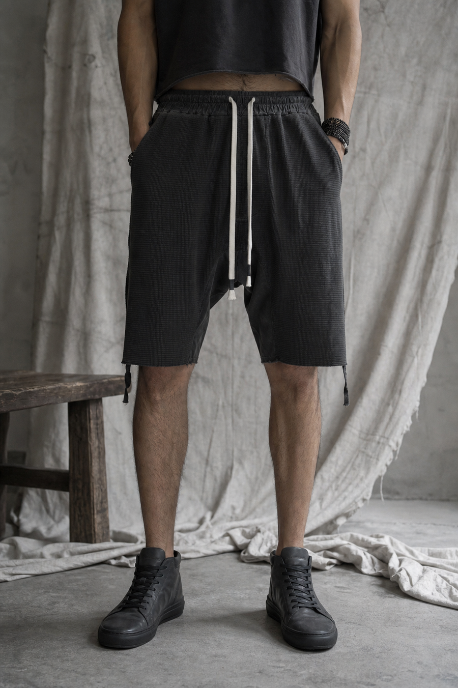 AITO Textured Drop-Crotch Shorts in Charcoal — front view on model, ivory knotted drawstring and hands in the deep side-seam pockets, hem above the knee