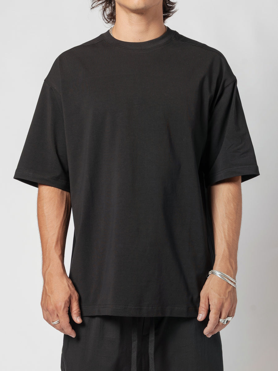 AITO Oversized Cotton T-Shirt in Black — front view of the torso, body turned a fraction to one side, arms loose and the boxy hem falling past the hip