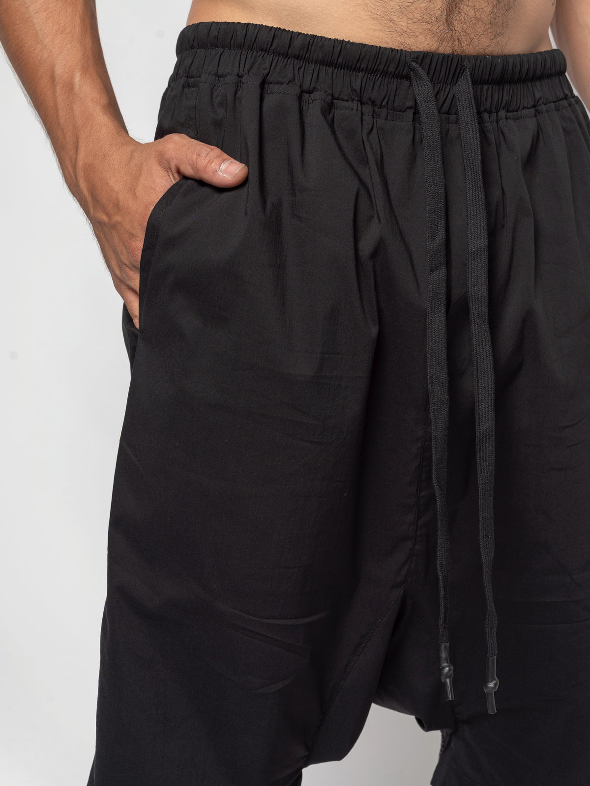 AITO Drop-Crotch Cotton Shorts in Black — close view of the front waist and hip with one hand pushed into the side pocket, drawcord tips hanging beside it