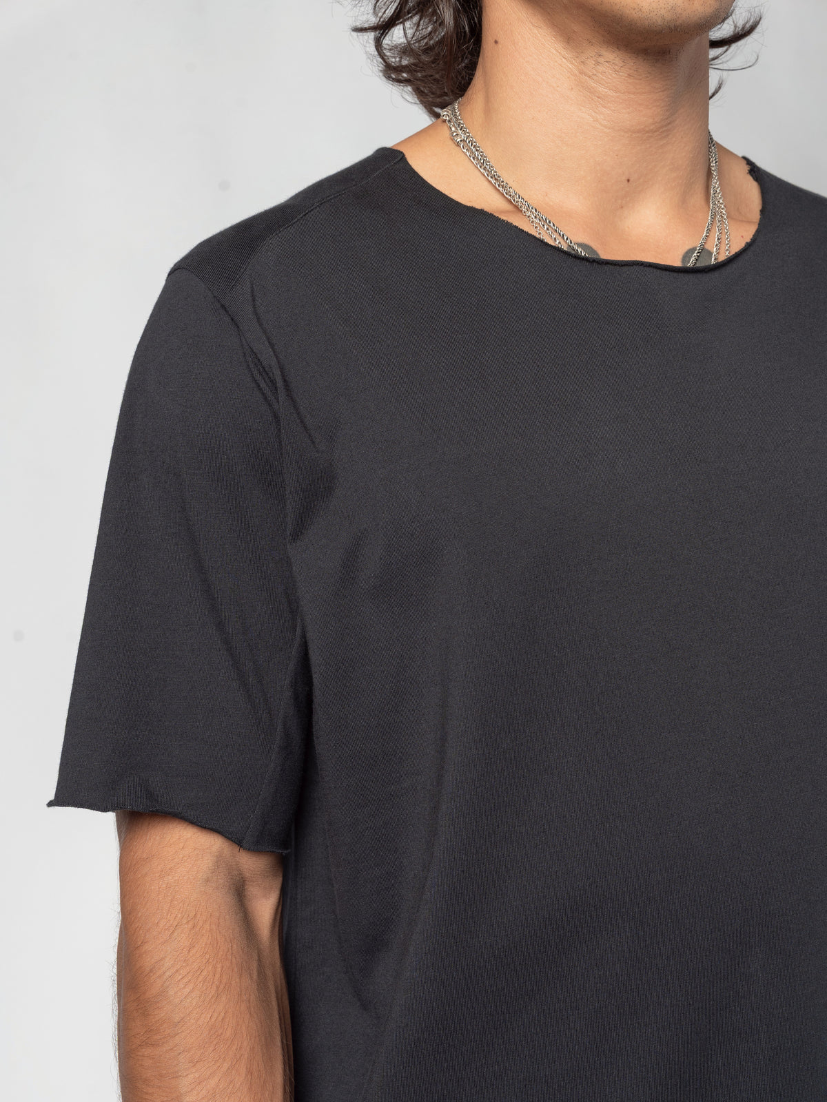 AITO Scar Stitch Cotton T-Shirt in Black — three-quarter view of the torso, the seam running from the neckline across the shoulder and out to the sleeve