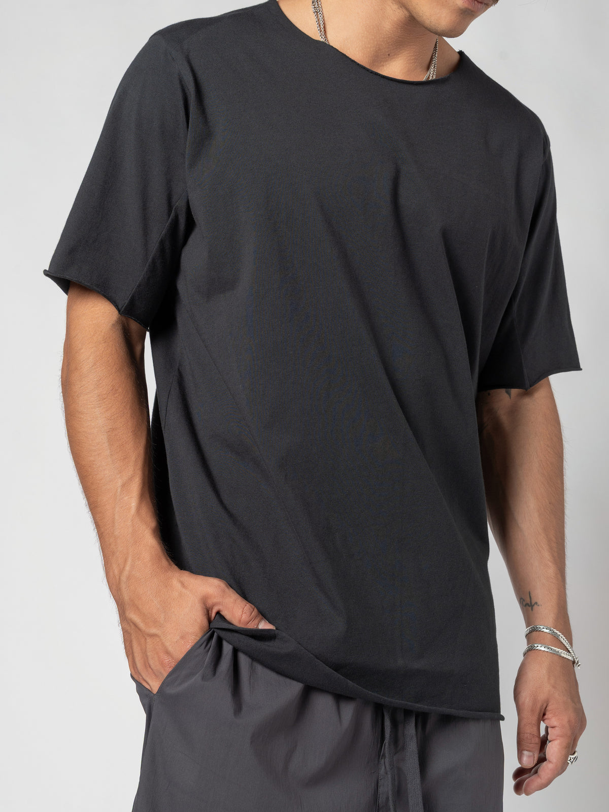 AITO Scar Stitch Cotton T-Shirt in Black — close-up of the front and side with a hand pushed into the pocket, the hem hanging past it