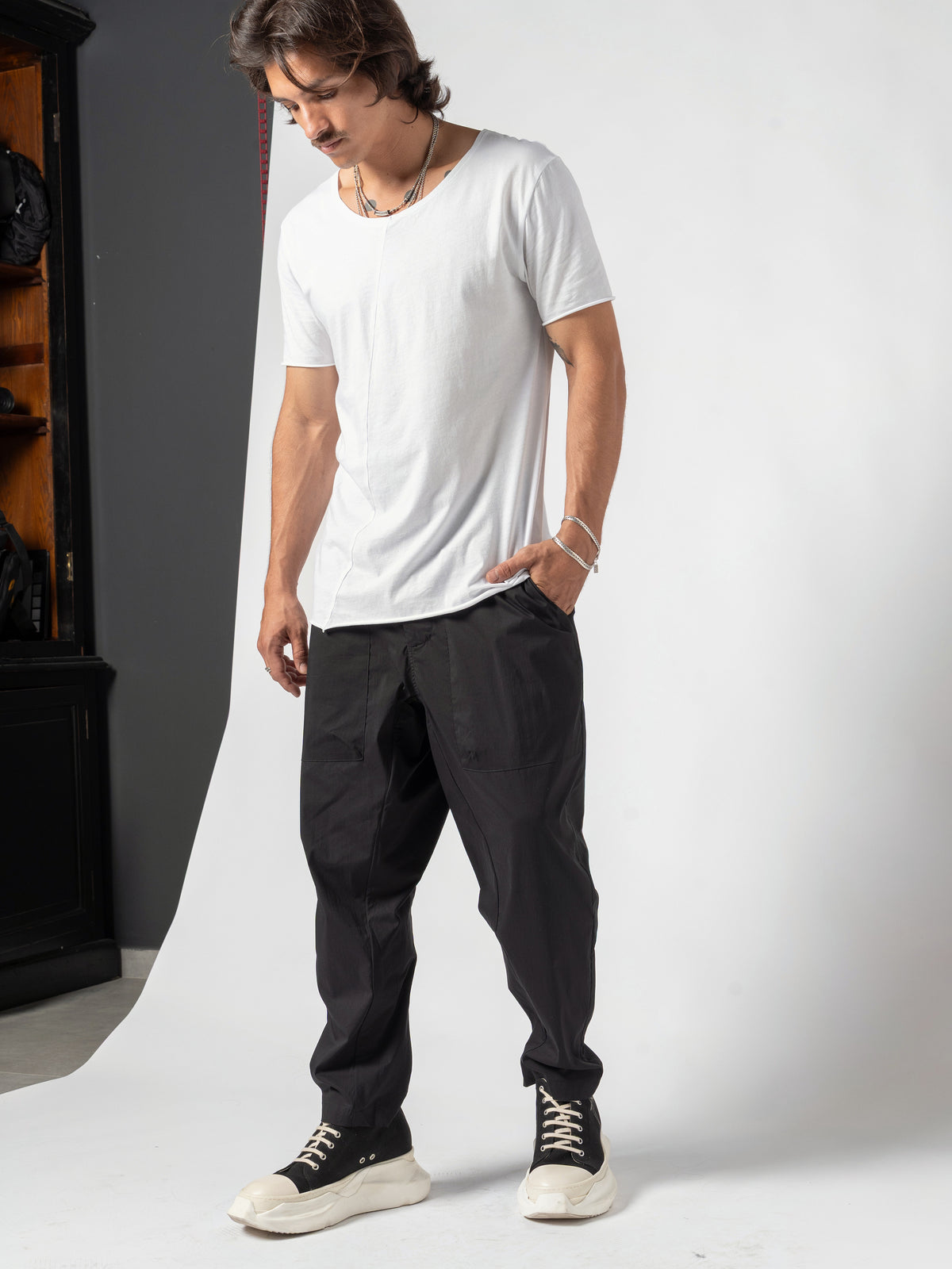 AITO Scoop Neck Cotton T-Shirt in White — full-length three-quarter, head lowered, one hand in the trouser pocket