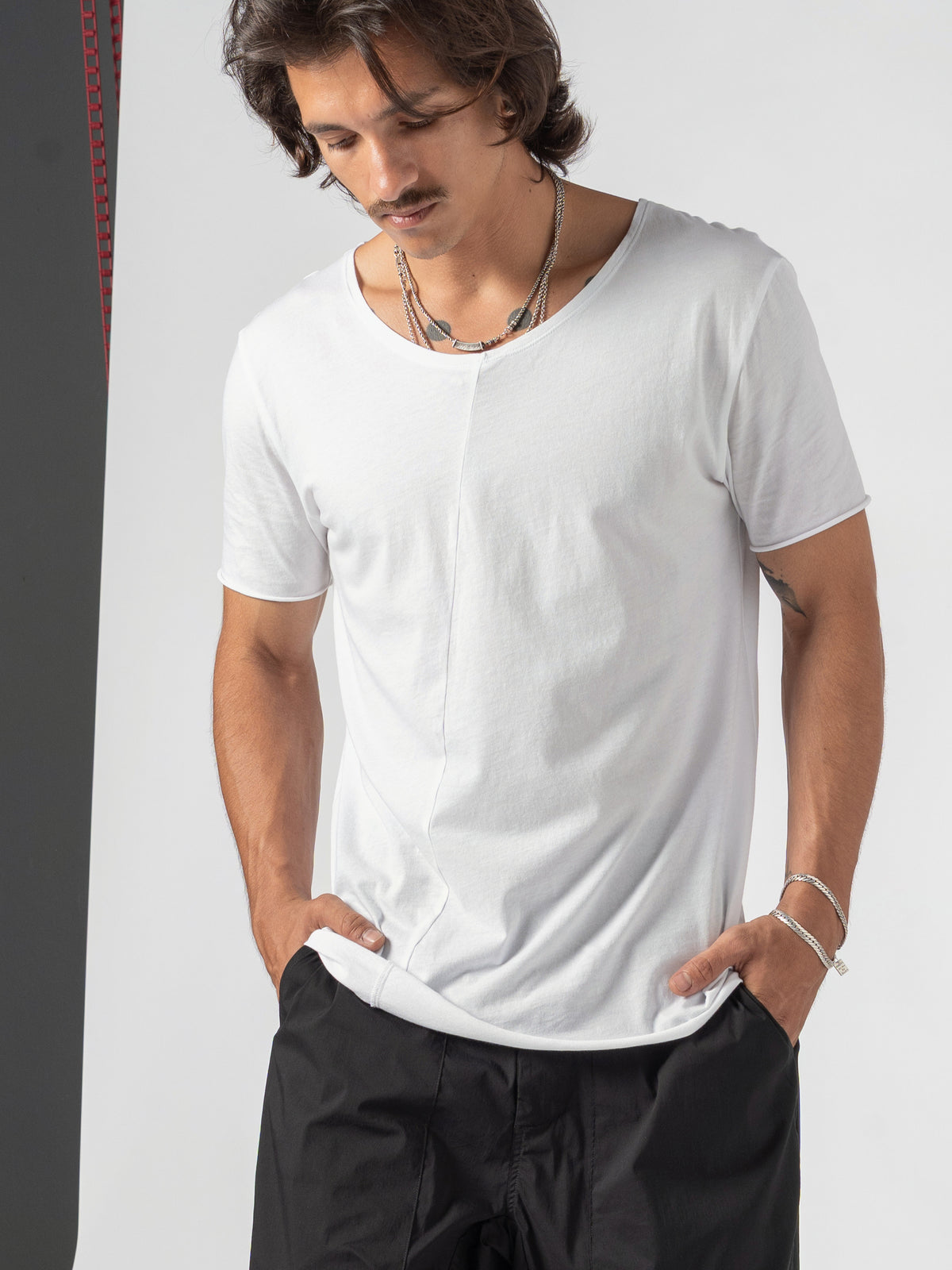 AITO Scoop Neck Cotton T-Shirt in White — torso close, head bowed, both hands pushed into the trouser pockets