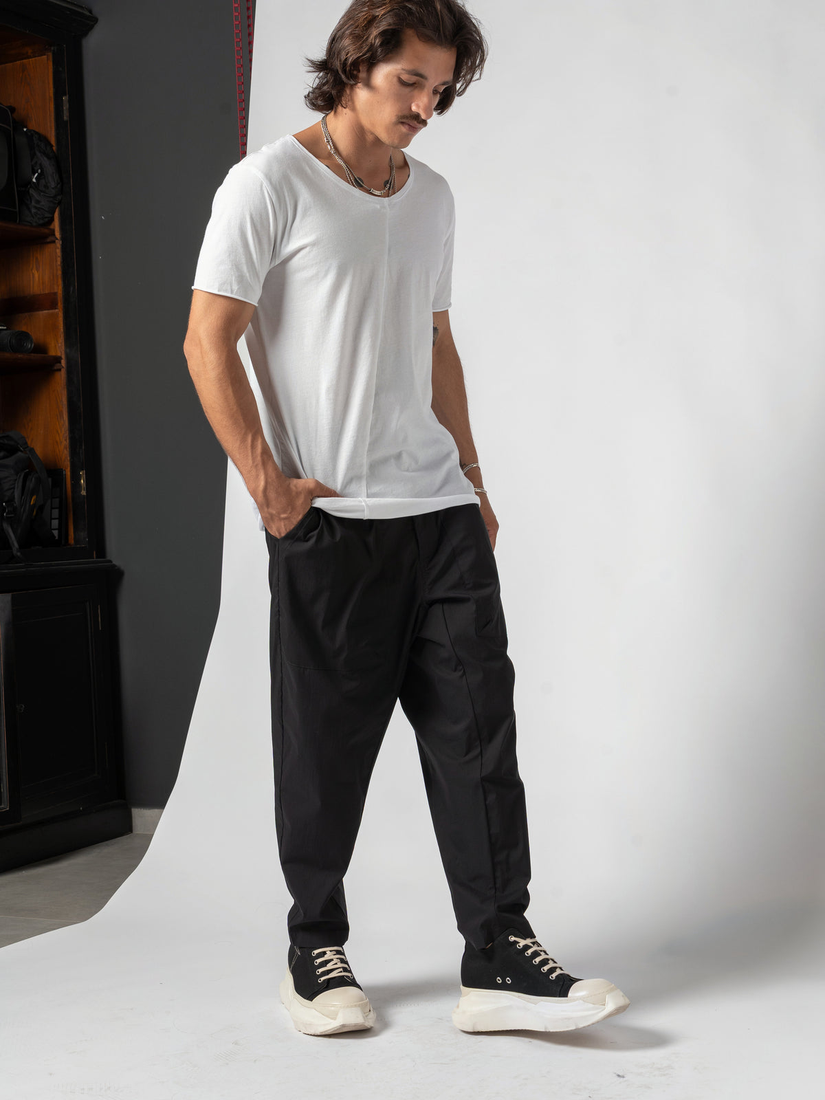AITO Scoop Neck Cotton T-Shirt in White — full-length three-quarter, legs crossed at the ankle, head turned away from the camera