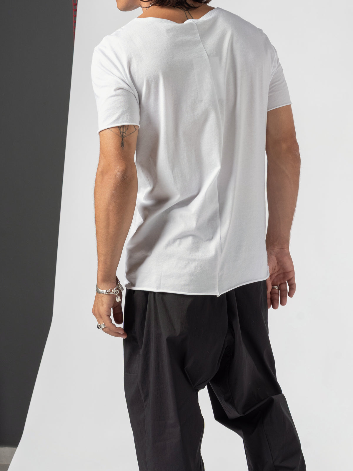 AITO Scoop Neck Cotton T-Shirt in White — back of the torso cropped above the neck, arms hanging, the hem dipping over the trousers