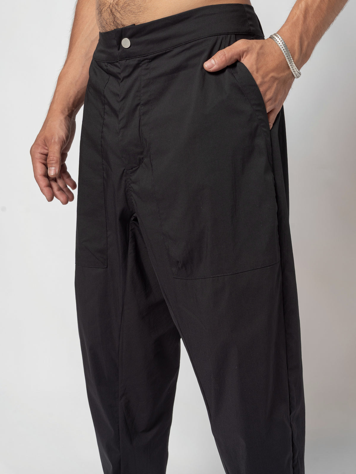 AITO Pleated Drop-Crotch Pants in Black — close-up of the front hip, the buttoned waistband and a hand slipped into the slanted side pocket