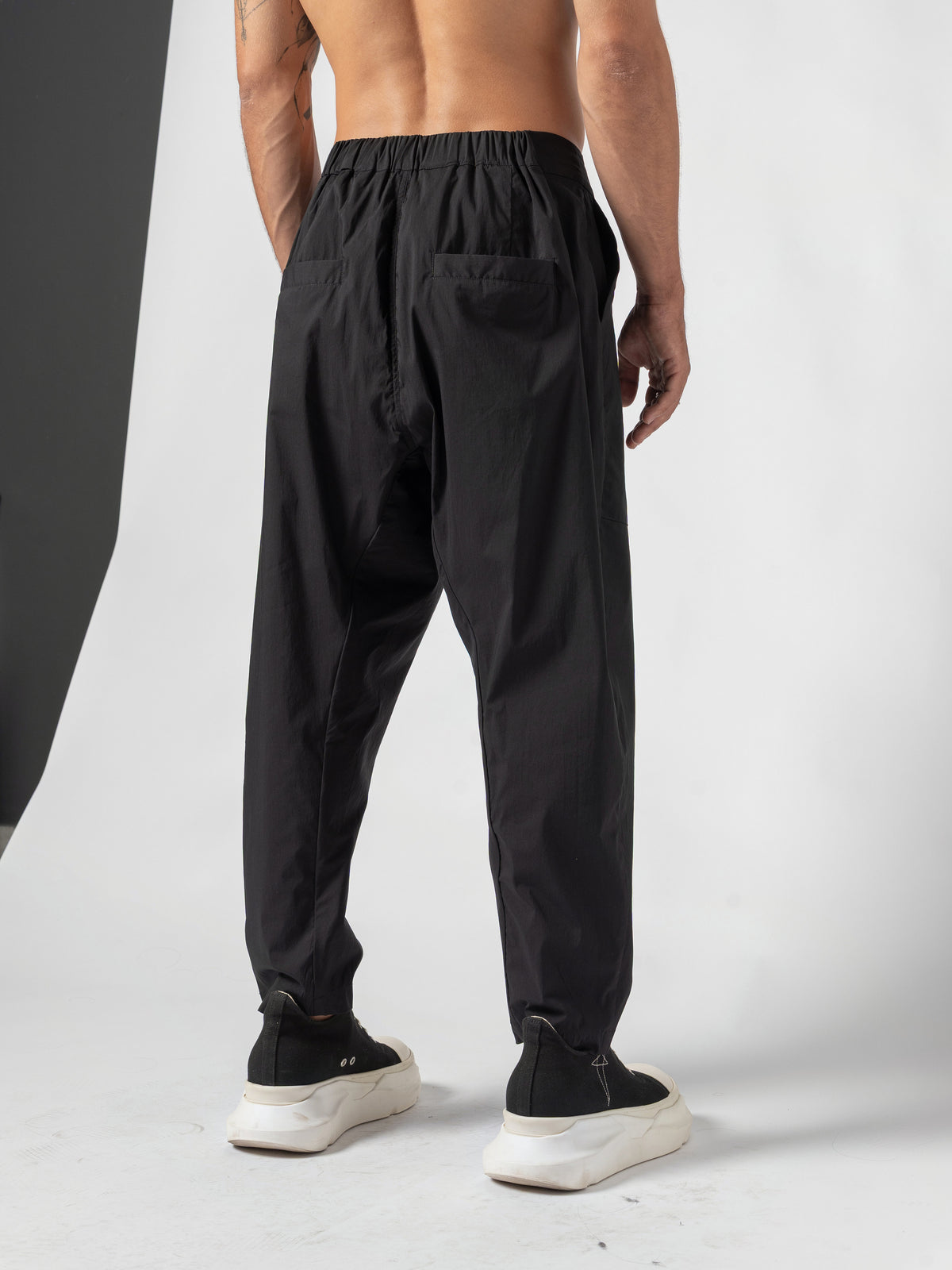 AITO Pleated Drop-Crotch Pants in Black — back three-quarter, the seat turned to camera with one patch back pocket in view