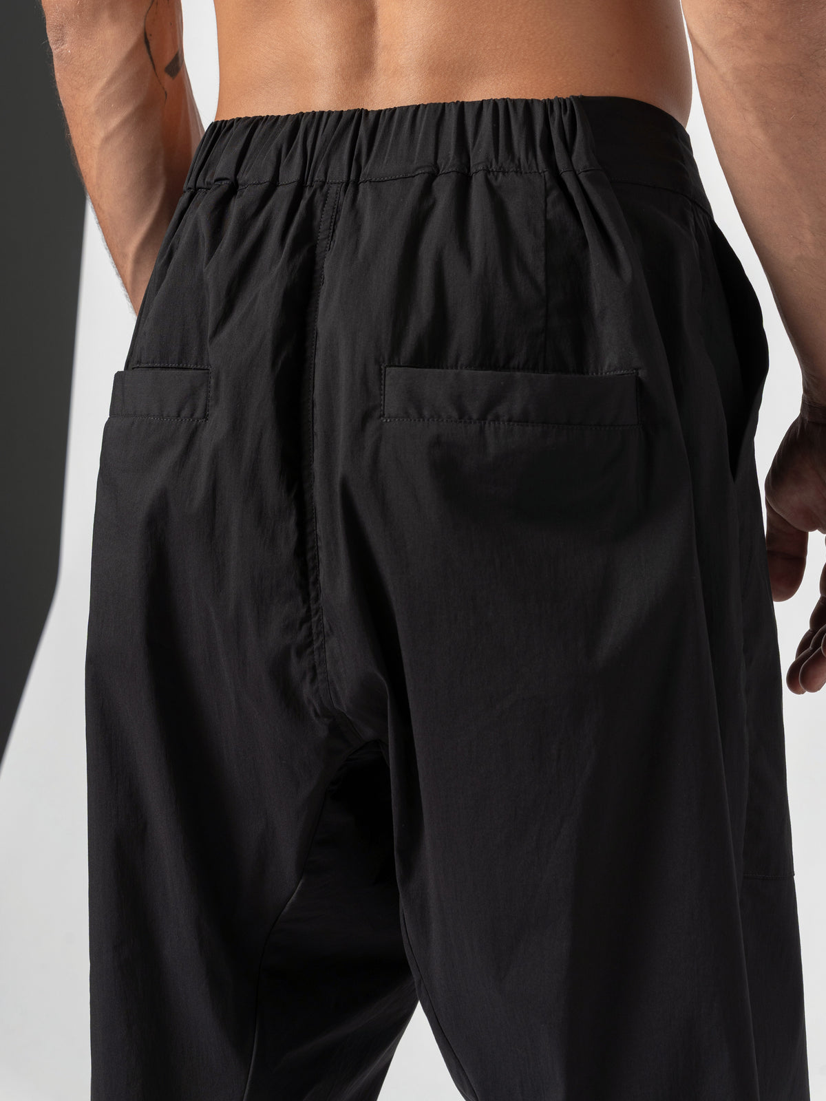 AITO Pleated Drop-Crotch Pants in Black — close-up from behind of the gathered waistband and patch back pockets, the dropped crotch seam below