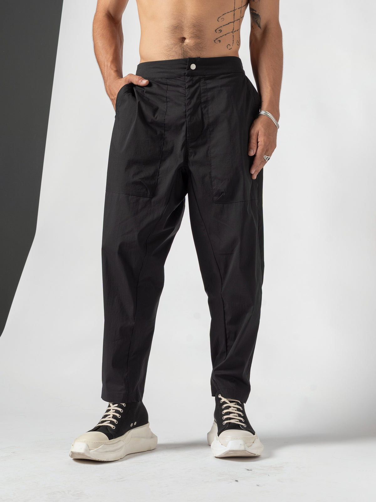 AITO Pleated Drop-Crotch Pants in Black — front view with one hand in the side pocket and the other arm relaxed, feet apart